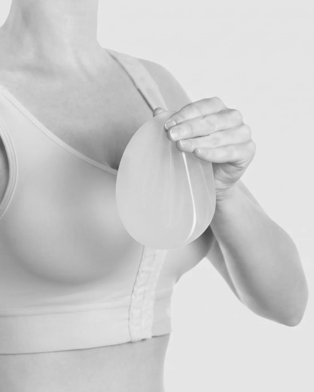 Mão segurando um implante mamário de silicone junto ao corpo, em sutiã cirúrgico